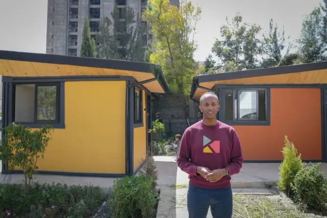 ቅዱስ ከተጣሉ ፕላስቲኮች ከተሰራ የሕጻናት ማቆያ ፊት ለፊት ቆሞ