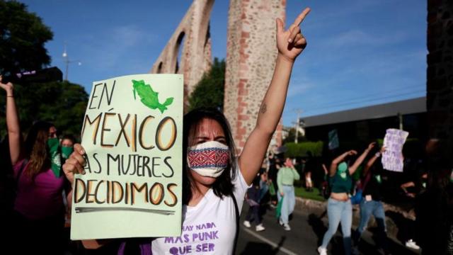 Manifestante erguendo o braço em protesto na rua, com cartaz dizendo: 'En México las mujeres decidimos'