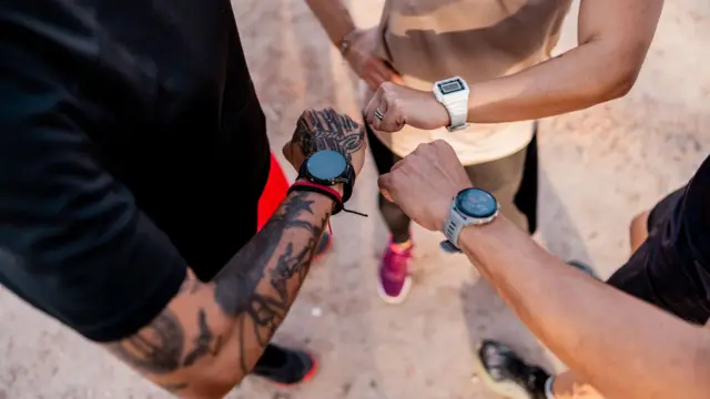 三名跑者低頭查看手腕上的智能手錶，照片從上方拍攝，焦點集中在他們的手臂與手腕