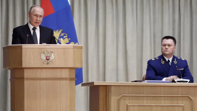 Президент на трибуне и человек в прокурорской форме сидит в президиуме