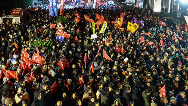 19 மார்ச் 2025 அன்று இஸ்தான்புல் நகராட்சிக்கு தலைமையகத்திற்கு வெளியே கொடிகளை அசைத்தபடி இரவில் கூடியிருந்த மக்கள்