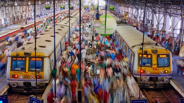 फोटोत मुंबई लोकल रेल्वे आणि प्रवासी दिसत आहेत.