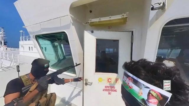 Rebeldes Houthi armados abrem a porta do convés de um navio