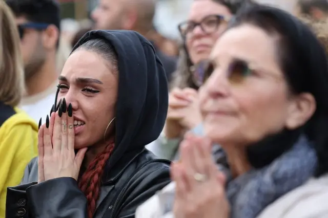 Una joven emocionada con las manos en el rostro en medio de varias personas