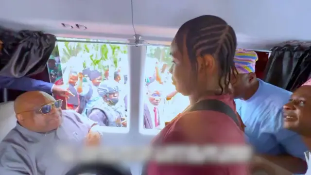 Gomina Ademola Adeleke joko sinu mọto laarin ero, o wọ asọ alawọ eeru, Oluwatosin Adejumo, to wọn asọ alawọ waini duro niwaju gomina, to n bi leere awọn ibeere.