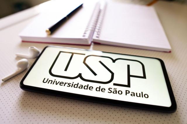 Celular com logo da USP em mesa de estudo