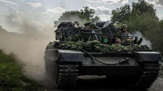 A foto mostra um tanque de guerra com soldados a bordo. 