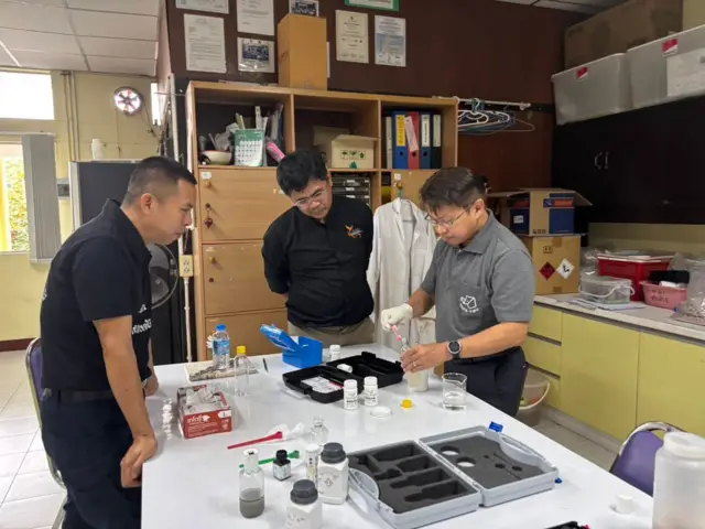 ผศ.ว่าน วิริยา (เสื้อดำคนกลาง) และคณะ ขณะกำลังนำตัวอย่างไปทดสอบหาสารหนูด้วยชุด test kit คุณภาพสูง ก่อนส่งตัวอย่างเข้าตรวจในห้องปฏิบัติการอีกรอบหนึ่ง