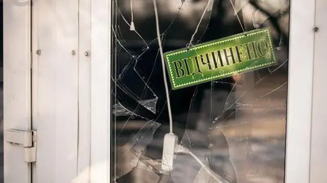 Розбите скло на дверях до магазину, на яких написано "Відчинено"