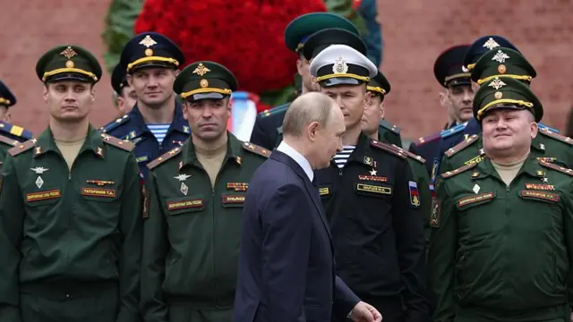 Vladimir Putin, bir  töreni sırasında esas duruştaki askerlerin yanından geçiyor. Aralarından bazıları Putin'in geçişini izliyor