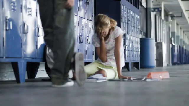 ከፊቷ የቆመ ሰው እግር እና ፊቷን በእጇ ሸፍና መሬት ላይ ተቀምጣ የምታለቅስ የምትመስል ወጣት ተማሪ