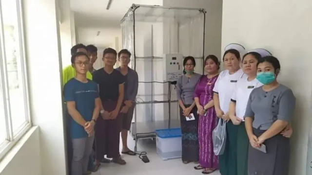 ပလက်စတစ်အကြည်ကို လေးဘက်လေးတန်ကာထားတဲ့ ပိုးသတ်ခန်း ဘယ်ဘက်မှာ ရပ်နေတဲ့ ကျောင်းသား ၅ ဦးနဲ့ ညာဘက်မှာရပ်နေတဲ့ ကျန်းမာရေးဝန်ထမ်း ၅ ဦး 