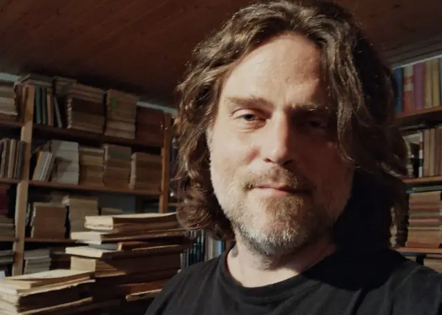 Un hombre en primer plano con libros detrás.