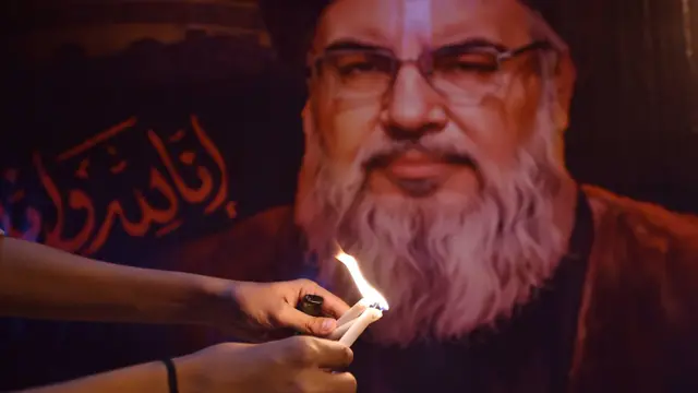 صورة تظهر شخصاً يشعل شمعة أمام صورة للأمين العام لحزب الله حسن نصر الله 