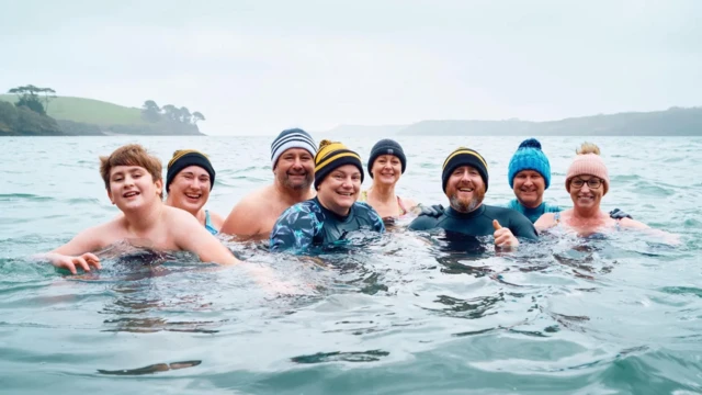 різні люди в шапках у холодній воді, позаду видно острів