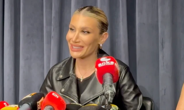 İrem Derici deri ceketiyle gülere konuşuyor, önünde mikrofonlar var.