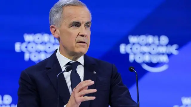 Прем’єр-міністр Канади Марк Карні в темному костюмі і синій краватці стоїть біля мікрофона на тлі синього банера з написом World Economic Forum
