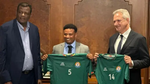 ዮሐንስ ከኢትዮጵያ እግር ኳስ ፌደሬሽን ፕሬዝዳንት ኢሳያስ ጂራ (በግራ) እና ከሳዑዲ አረቢያው ክለብ አል ናስር ዋና ስራ አስፈጻሚ ጊዶ ፊንጋን (በስተቀኝ) ጋር