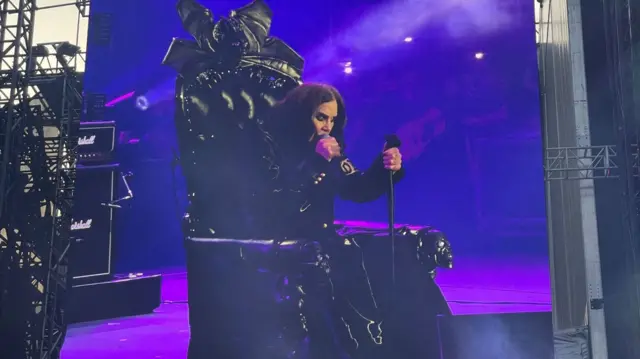 Оззи Осборн сидит в кресле во время выступления на прощальном концерте