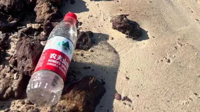 Garrafa de água com rótulo vermelho e branco em praia com pedras