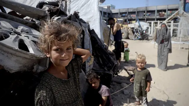 Derme çatma bir kamp yerinde ikisi sarışın üç çocuk kameraya bakıyor