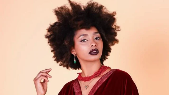 Foto de busto da modelo e criadora de conteúdo Houda Fonone, vestindo uma blusa vermelha escura, um colar de contas vermelhas e brincos verdes.