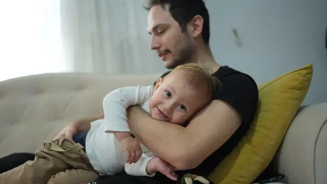 رجل يحمل طفلاً على رجله والطفل يبتسم