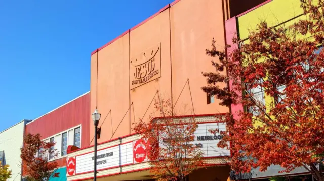 El teatro Lamplight, en una calle central con una calzada con árboles pequeños y lámparas, tiene un letrero sobre su fachada color ladrillo que lee: "Jesús sobre todas las cosas"
