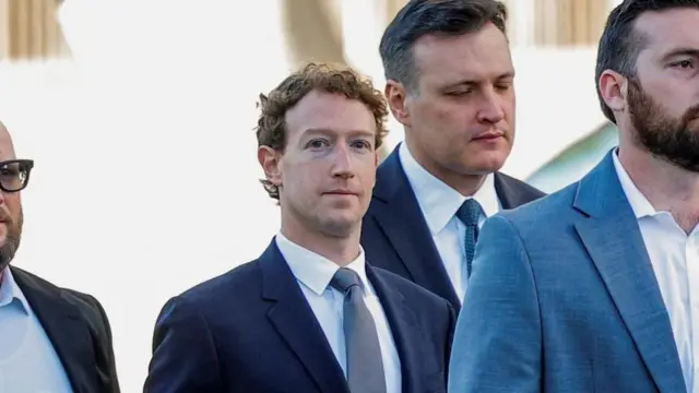 Zuckerberg resmi kıyafetli birkaç adamla birlikte bir alanda yürüyor.