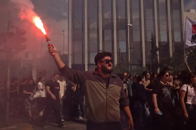 muškarac drži baklju tokom štrajka radnika u Atini