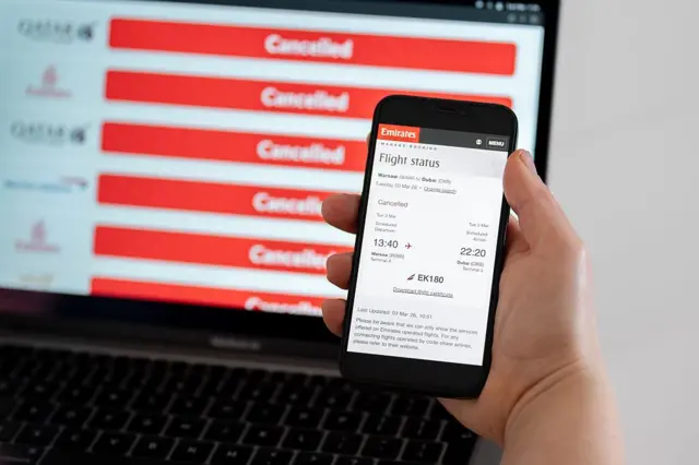 يظهر على شاشة هاتف محمول إشعار بإلغاء رحلة تابعة لشركة طيران الإمارات، فيما يظهر على شاشة كمبيوتر موقع يعرض رحلات ملغاة، وذلك في مدينة كراكوف ببولندا في 3 مارس/آذار 2026.