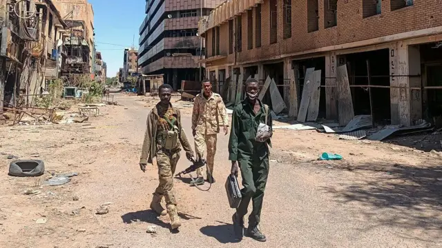 Троє чоловіків ідуть вулицею між зруйнованих будинків у Хартумі