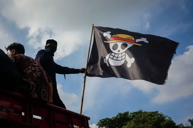 Seorang demonstran memegang bendera bajak laut dari anime Jepang One Piece saat mereka memblokir jalan di depan kantor bupati di Pati, Jawa Tengah, pada 31 Oktober 2025.