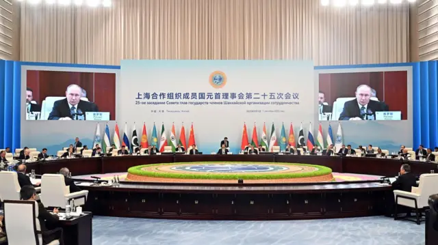 Лидеры стран ШОС сидят за большим столом под надписью на китайском и русском языках