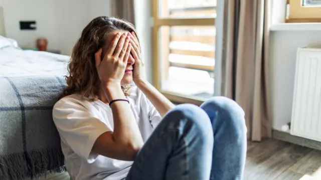 امرأة تغطي وجهها بيديها وتجلس على الأرض 