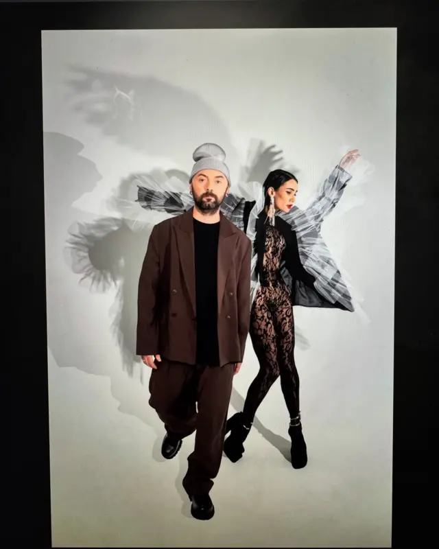 Клименко в коричневому костюмі та сірій шапці та Норова у прозорому мереживному комбінезоні та пілджаку