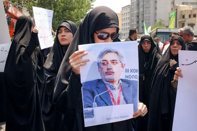 Tahran'daki protestolarda bir kadın saldırılarda öldüğüne inanılan Nükleer Bilim ve Teknoloji Araştırma Enstitüsü Başkanı Seyid Amir Hüseyin Fakhi'nin fotoğrafını taşıyor. Arkada siyah çarşaf içerisinde başka kadınlar görülüyor.