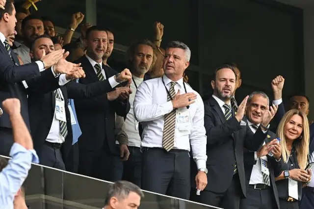 Saadettin Saran kalabalık bir alanda destekçilerini selamlıyor, herkes koltuklardan kalmış ayakta. 