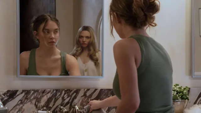 Uma cena de "A Empregada" mostra Sydney Sweeney de costas para a câmera, mas com a frente de seu corpo refletida num espelho. Ela está olhando para Amanda Seyfried, que aparece atrás dela no reflexo. Sweeney veste uma regata verde e Seyfried, uma blusa branca. 
