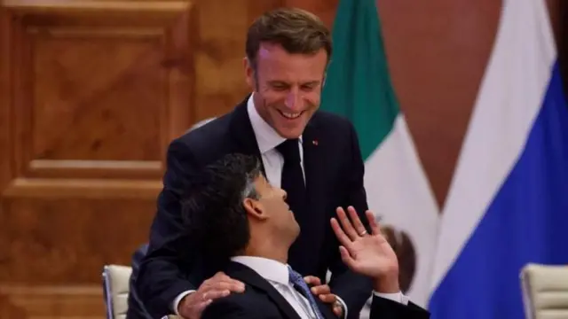 Emmanuel Macron e Rishi Sunak se cumprimentando e sorrindo