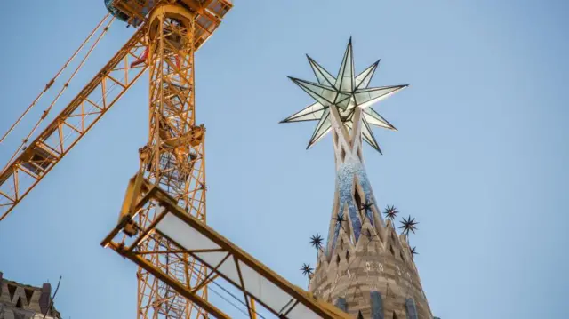 Una grúa de construcción amarilla se alza junto a la parte superior de una torre, que tiene una estrella de 12 puntas.