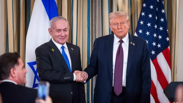 Waziri Mkuu wa Israel Benjamin Netanyahu (kulia) akipeana mkono na Rais wa Marekani Donald Trump mbele ya waandishi wa habari. Nyuma yao kuna bendera zao za kitaifa.