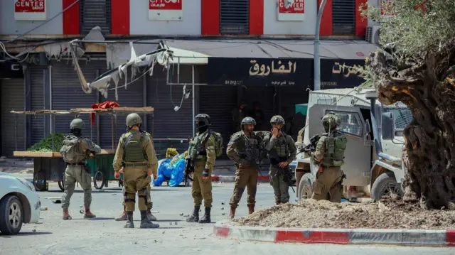 جنود إسرائيليون يقومون بدورية عند تقاطع طرق في مدينة جنين، الضفة الغربية، في 27 مايو/أيار 2025. اقتحمت قوات الاحتلال الإسرائيلي عدة مواقع، بما في ذلك محلات صرافة، وصادرت مبالغ مالية كبيرة، واعتقلت أفرادًا يُزعم ارتباطهم بفصائل المقاومة الفلسطينية. 