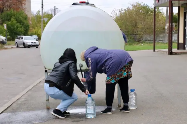 Дві жінки набирають воду біля каністри з водою 