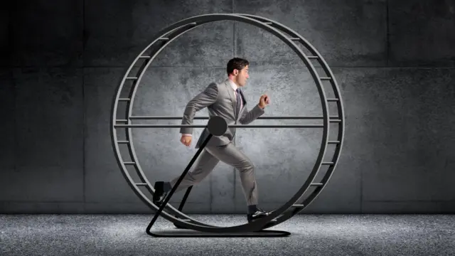 Homem de terno e gravata correndo em uma roda de hamster gigante