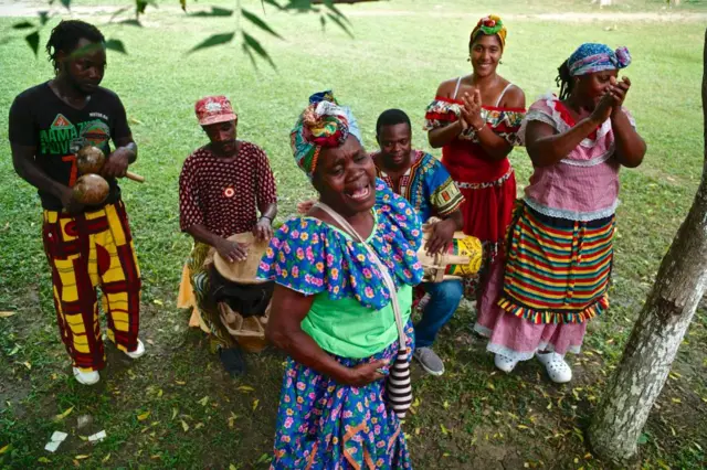 Músicos y cantantes, hombres y mujeres, de San Basilio de Palenque en coloridos atuendos tocando y cantando