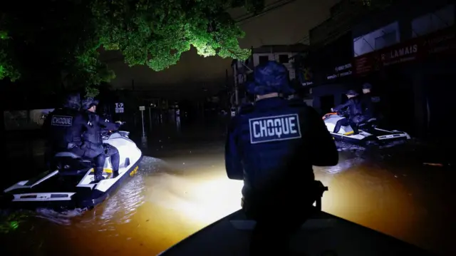 Fotografia colorida mostra policiais fazendo ronda365 bet cadastrojet ski à noite 365 bet cadastrouma rua alagada