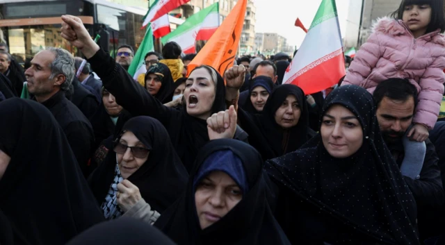 Fotoğrafta siyah çarşaflı çok sayıda kadın var. Bazısı slogan atar şekilde ağızlarını açmış durumda. Arka tarafta erkekler ve bayraklar görünüyor.