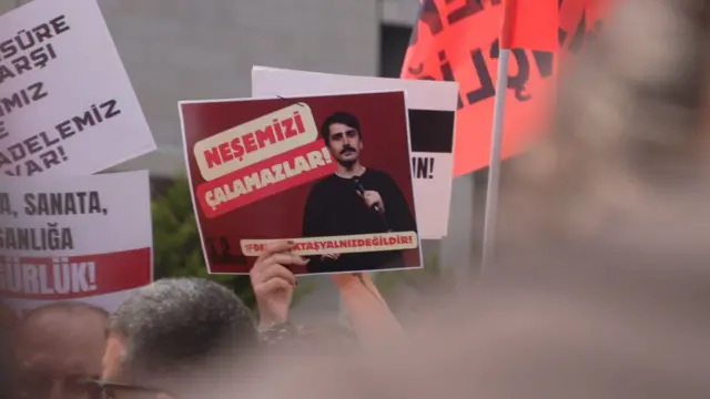 Kalabalık içinde Deniz Göktaş fotoğrafı üzerinde "Neşemizi çalamazlar... Deniz Göktaş yalnız değildir" yazılı dövizi tutan bir el