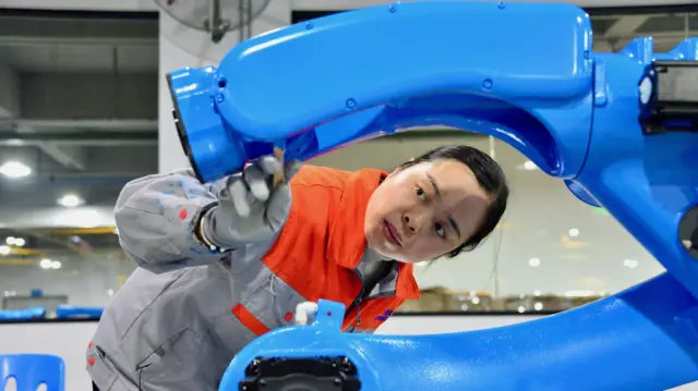Genç bir kadın mavi bir robot kolunu inceliyor.